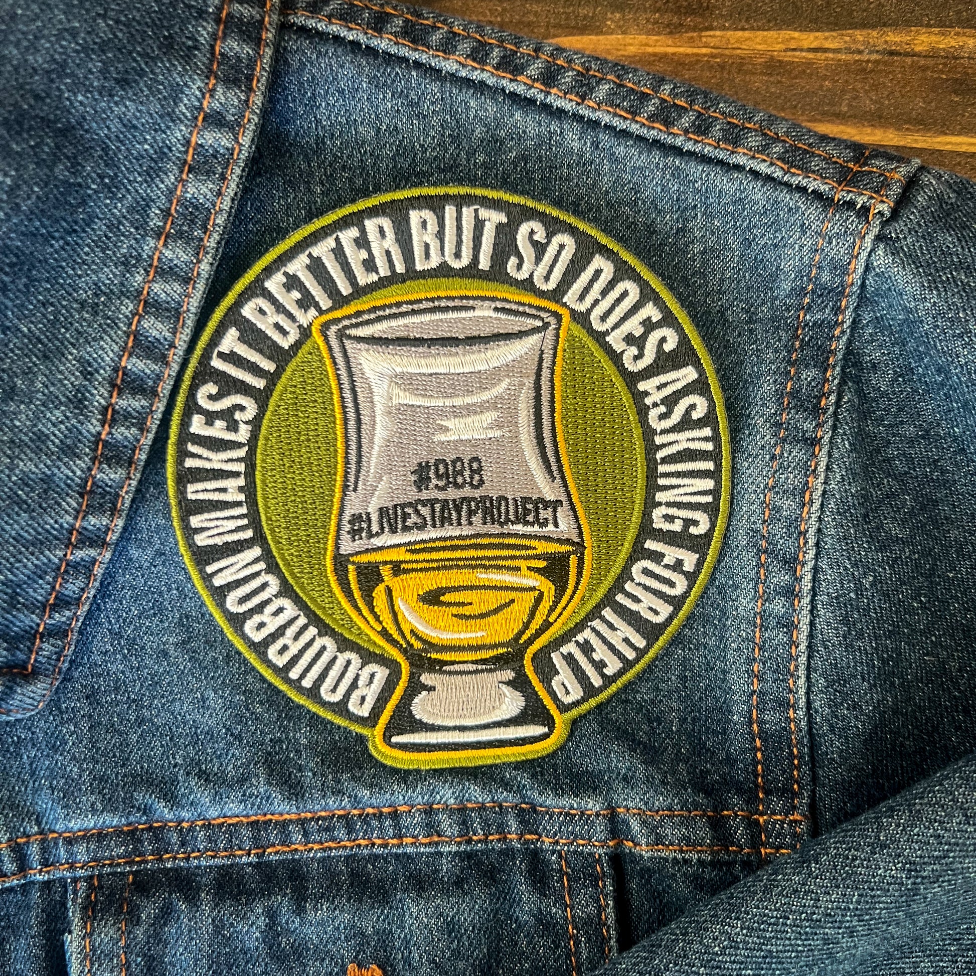 Shows embroidered sew-on patch that reads, "Bourbon makes it better but so does asking for help" on a denim jacket